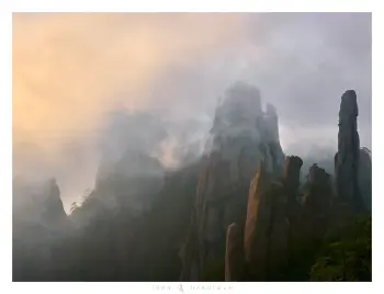 A photo of incredible mountain peaks with sunlit mist wrapping around them.